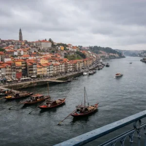 Vista panorámica del Cais da Ribeira y el río Duero en Oporto bajo un cielo nublado, resaltando la arquitectura tradicional y los barcos rabelos.