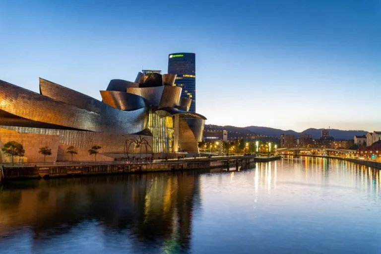 El Museo Guggenheim Bilbao, una joya arquitectónica que te espera en tu ruta por el norte de España, ilumina la ría al atardecer.